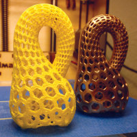 3D printed yellow plastic draft of the "Klein Bottle Opener" next to a finished model printed in brass and bronze from Shapeways.