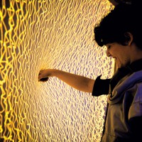 jumbled squiggles of yellow light cover a flexible membrane as a person pushes their fist into the center