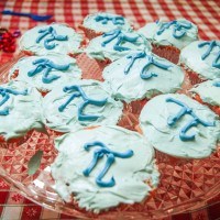 A plate of light blue cupcakes with the mathematical symbol for pi frosted onto them.