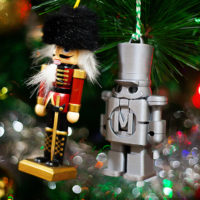 Two christmas ornaments side by side, one traditional nutcracker red and black, one 3D printed grey Makey nutcracker in a christmas tree.