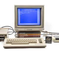 A beige Commodore 64 computer terminal on a white backdrop. The program for "Hello World" is on the screen.