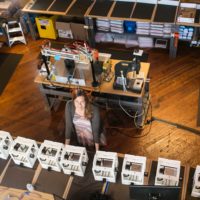 Danielle Applestone stands surrounded by tables with CNC mills looking up.